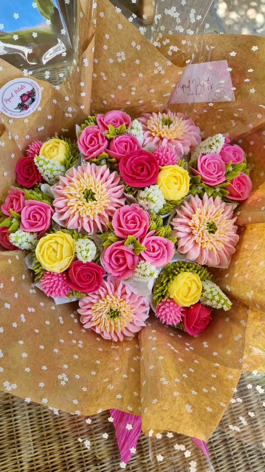 A cupcake bouquet of piped buttercream roses and dahlias in pink and yellow