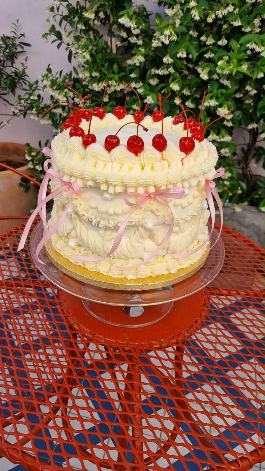Vintage-style piped buttercream cake topped with cherries and ribbon